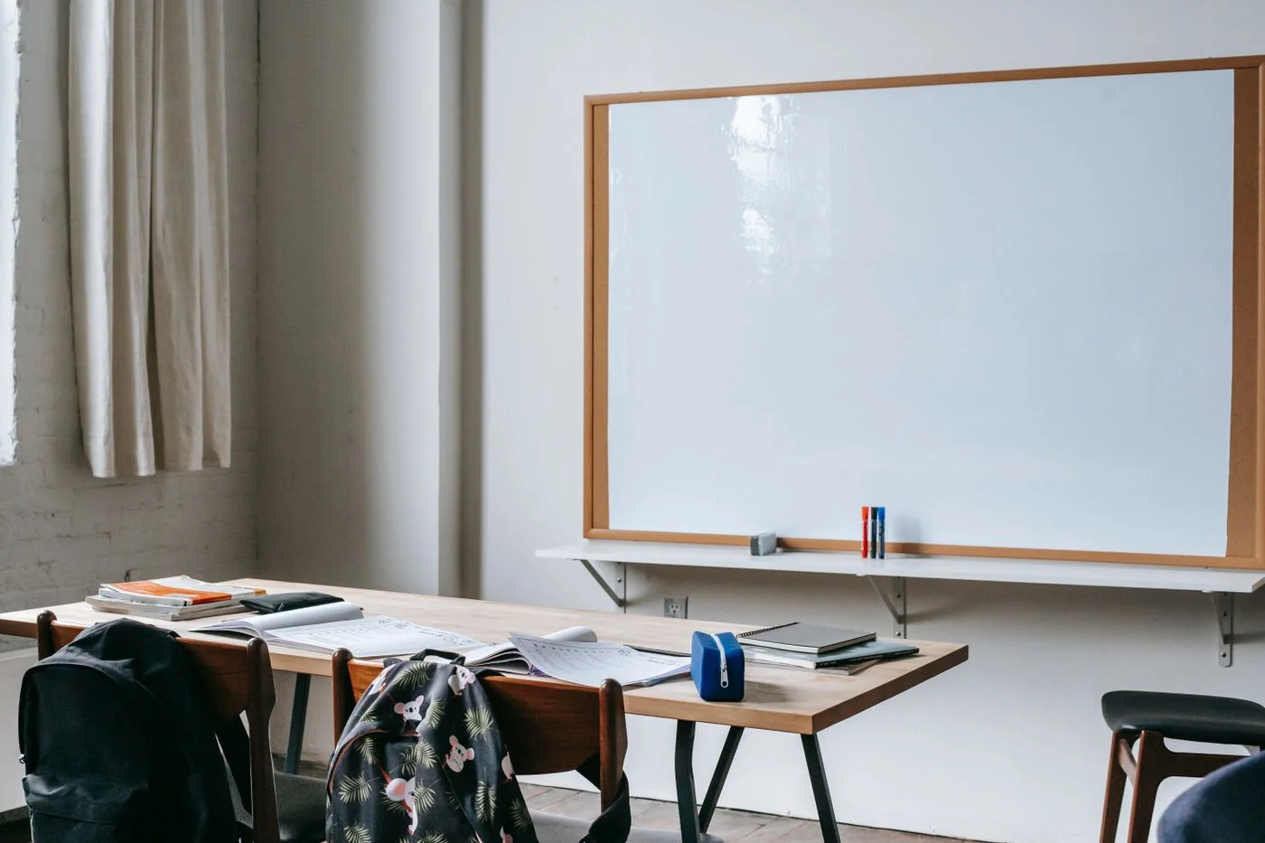 Una mesa con cuadernos y una pizarra en un aula con luz natural