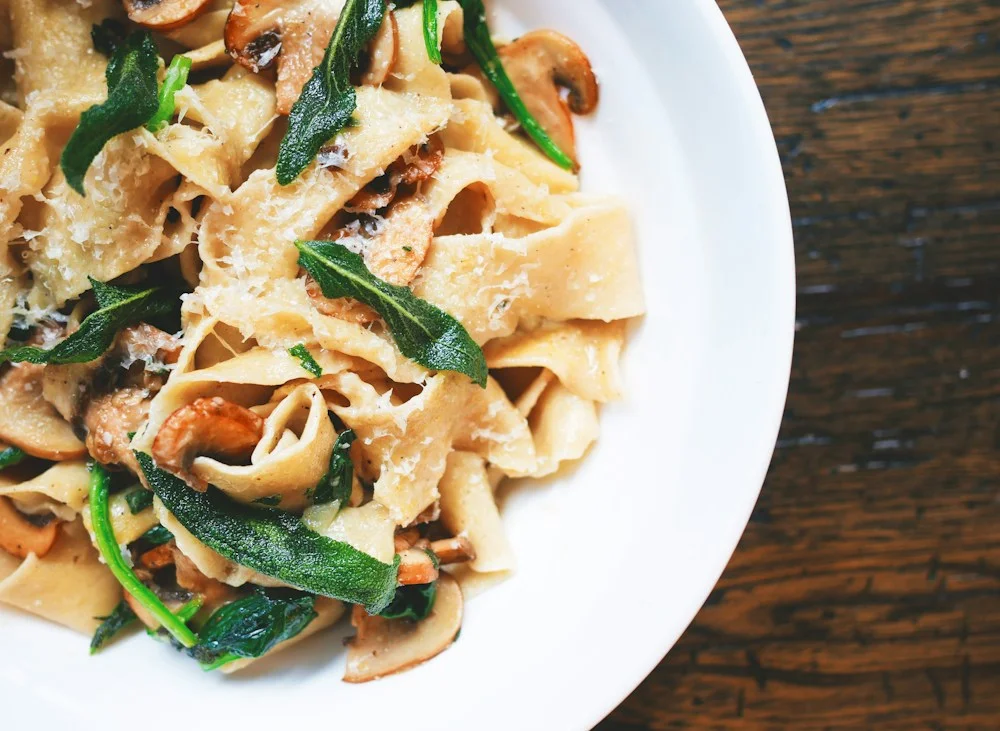 Pappardelle con setas, salvia y queso rallado sobre un plato blanco