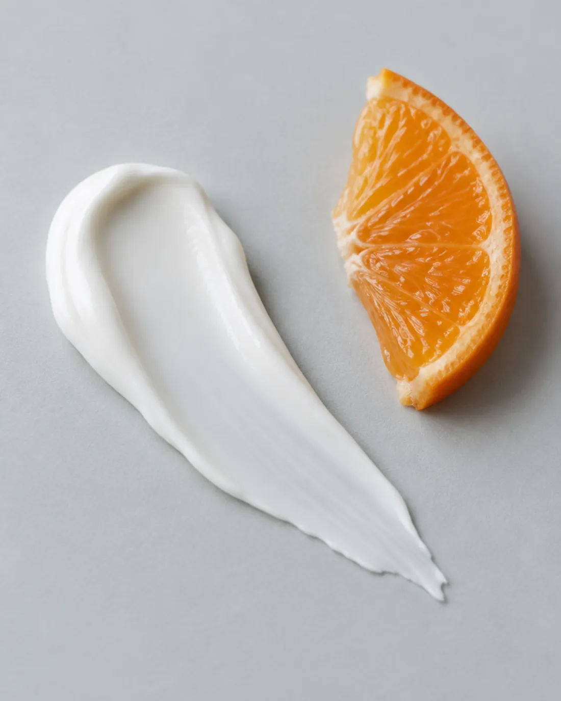 Un trazo de crema blanca junto a un gajo de mandarina sobre una superficie gris clara